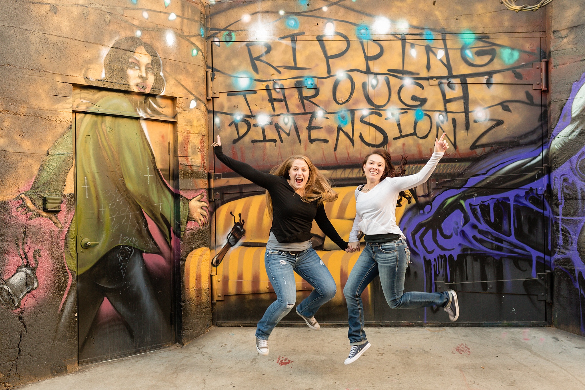 Same-Sex couple jumping in front of a mural. Jessica & Caity’s Same-Sex Engagement Session at 10 Barrel Brewery & RiNo District by Colorado Engagement Photographer, Jennifer Garza. 10 Barrel Brewery Engagement, Brewery Engagement Photos, RiNo District Engagement Photos, RiNo District, RiNo Engagement Photography, Denver Engagement Photography, Denver Engagement, Colorado Engagement Photography, Urban Engagement Photos, Same-Sex Engagement Photography, Same-Sex Engagement Photos, Same-Sex Marriage, Love is Love, LGBTQ